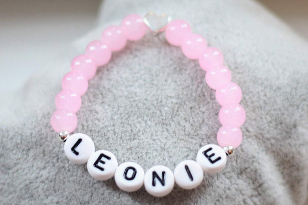 Namensarmband in rosa pink mit silberfarbenem Herz in der Mitte und zwei kleinen silbernen Perlen neben dem Namen