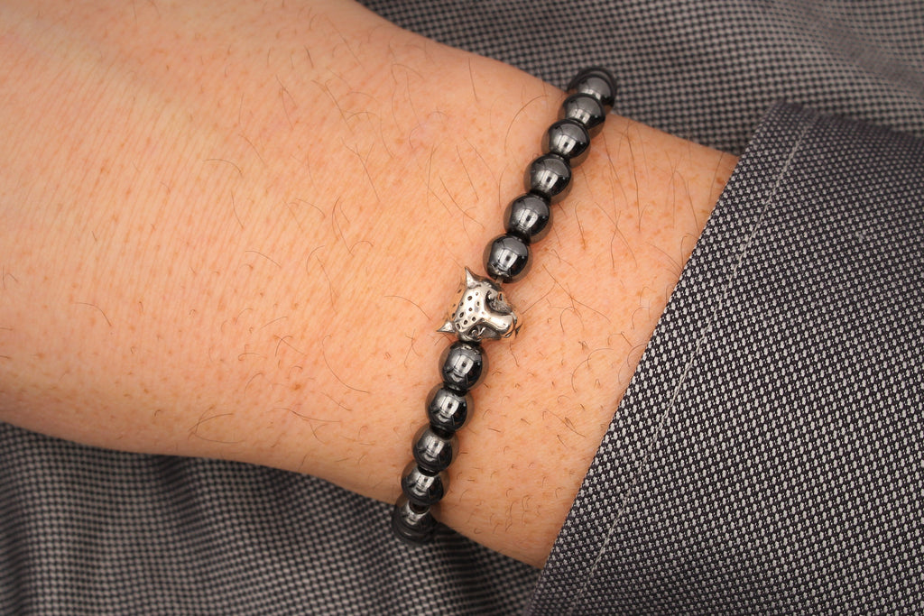 graues Herrenarmband Leopard aus Hämatiten Perlen mit silberfarbenem Leopardenkopf als Symbol in der Mitte am Handgelenk des Mannes getragen