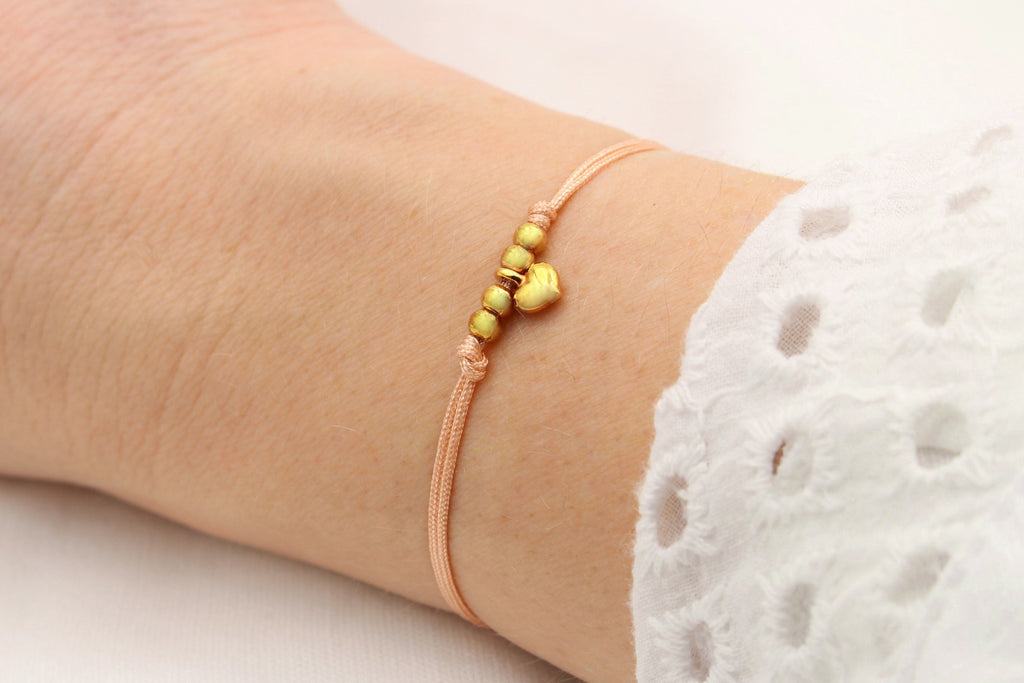 Filigranes apricot farbenes Armband mit goldfarbenem Herz Anhänger und Perlen am Handgelenk der Frau getragen