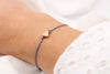 dunkel graues Makramee Armband mit rosegoldfarbenem Herz am Handgelenk der Frau getragen