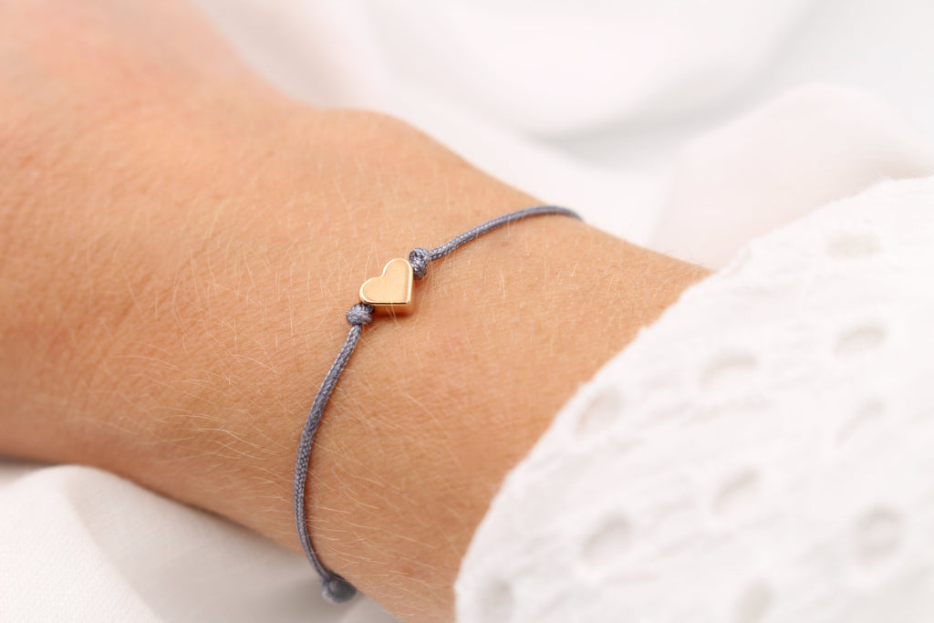dunkel graues Makramee Armband mit rosegoldfarbenem Herz am Handgelenk der Frau getragen