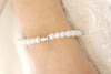 weißes Perlenarmband mit Ichthys Fisch als Symbol am Handgelenk des Kommunion Mädchen getragen