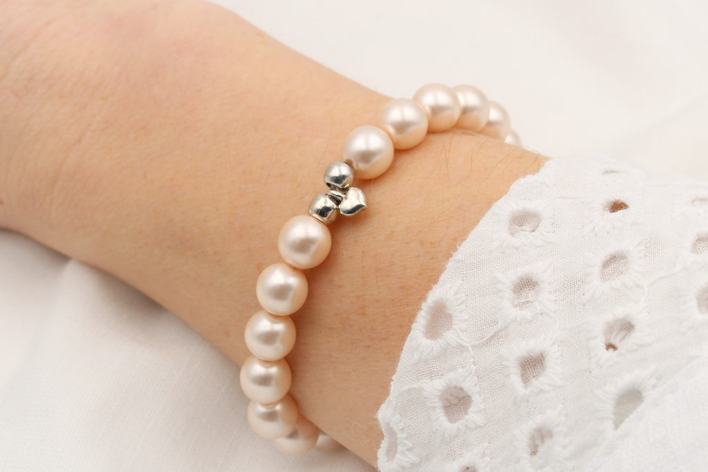 Armband aus rosa perlmutt farbenen Perlen mit silbernem Herz Anhänger am Handgelenk der Frau getragen