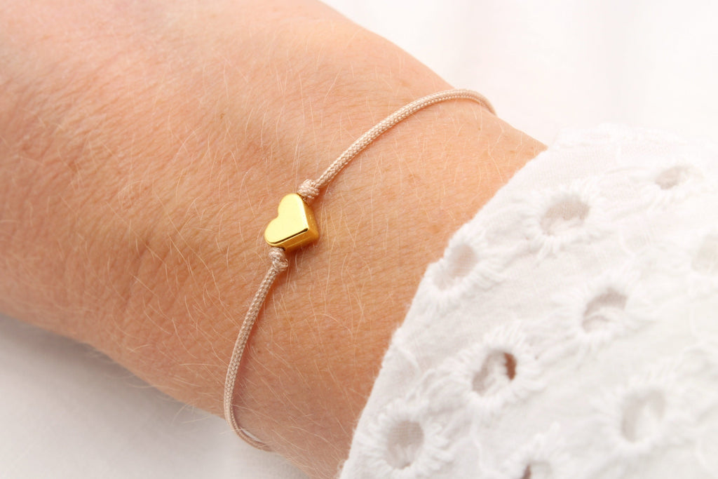Rosenholzfarbenes Makramee Armband mit goldfarbenem Herz am Handgelenk der Frau getragen und Schiebeknoten Verschluss zum verstellen
