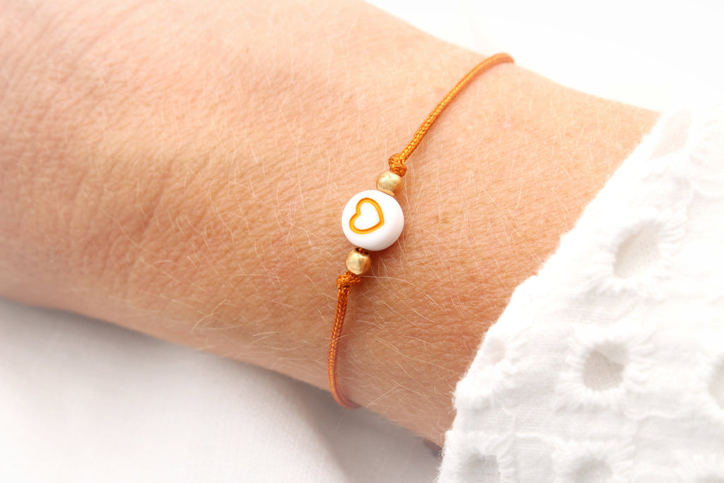 oranges Schulkind Armband mit weißer Herzperle am Handgelenk getragen