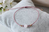 schlichtes Makramee Armband in Aubergine Red und kleinen Perlen auf einem grauen Kissen gelegen